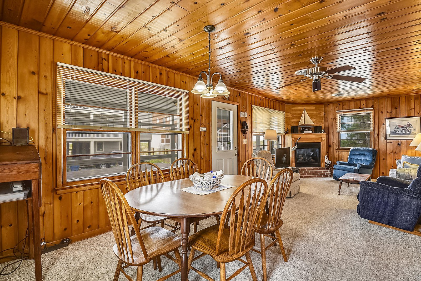 Step into the warmth of knotty pine walls and vaulted ceilings, where a classic dining table invites you to gather for meals. Relax in the cozy sitting area by the brick fireplace, surrounded by timeless comfort and homey charm.