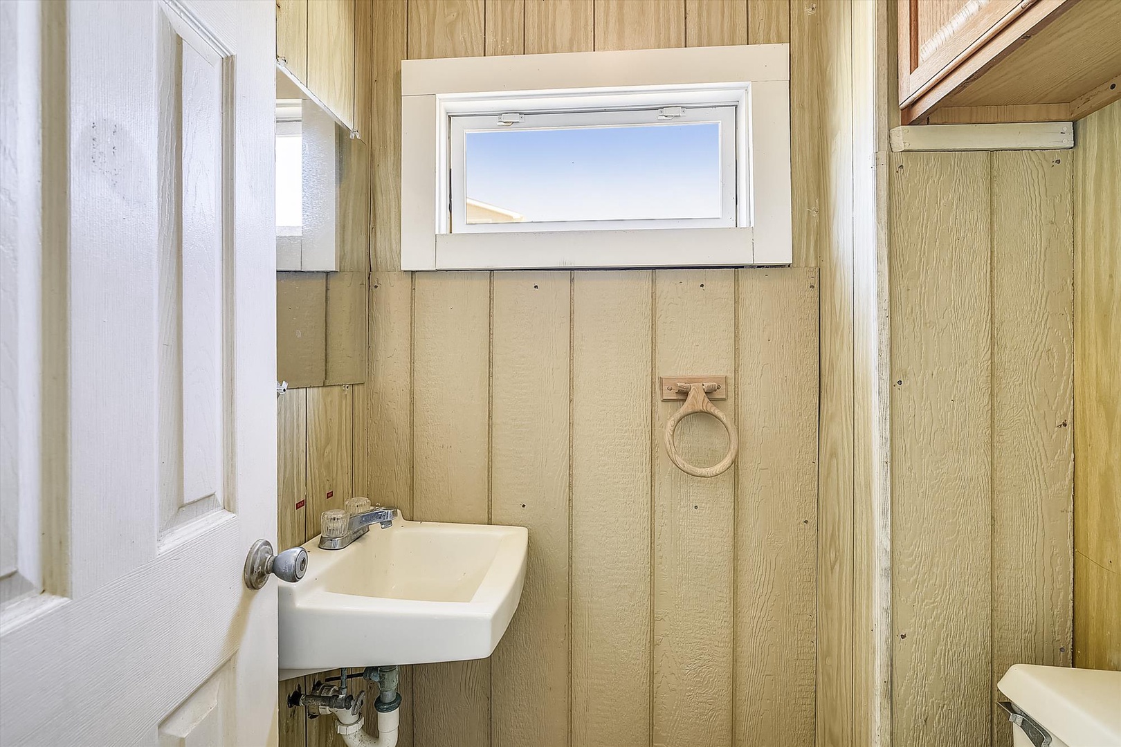 Your cozy bathroom features warm wood paneling and natural light from the window above, creating a charming and inviting space for your stay.