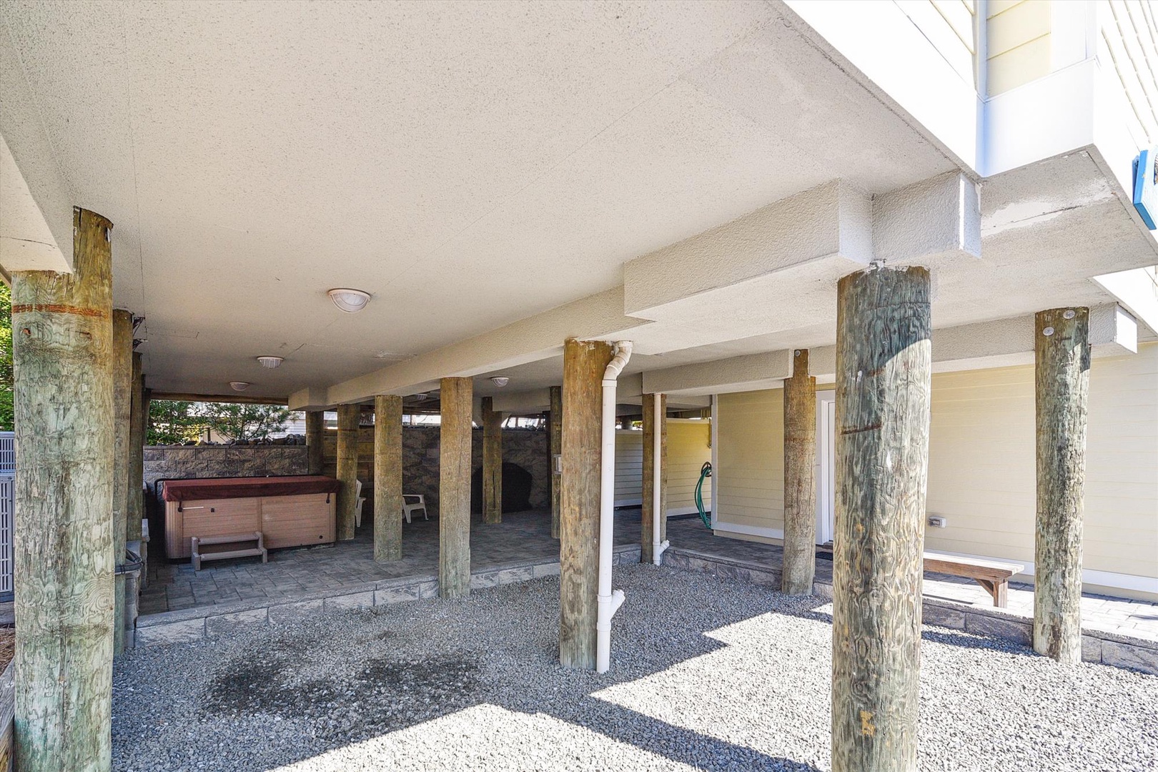 Covered outdoor space featuring rustic log posts, gravel flooring, and a private hot tub, with ample sheltered room for relaxing in any weather.