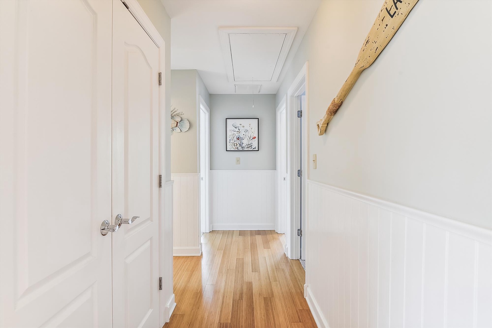 Soft natural light fills this welcoming hallway, where warm wood floors meet coastal-inspired decor. A charming paddle accent and framed botanical art create a serene, beachy atmosphere throughout your stay.