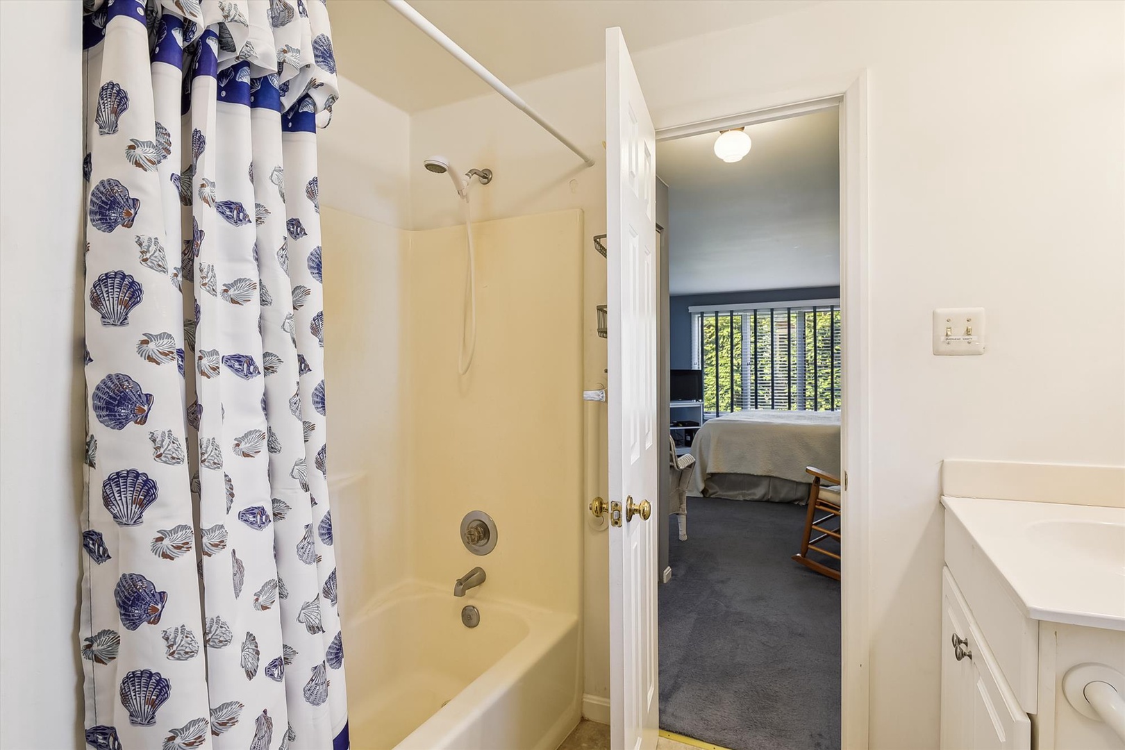 Your private bathroom features a cheerful seashell-patterned curtain and refreshing tub-shower combo, connecting seamlessly to your cozy bedroom retreat.