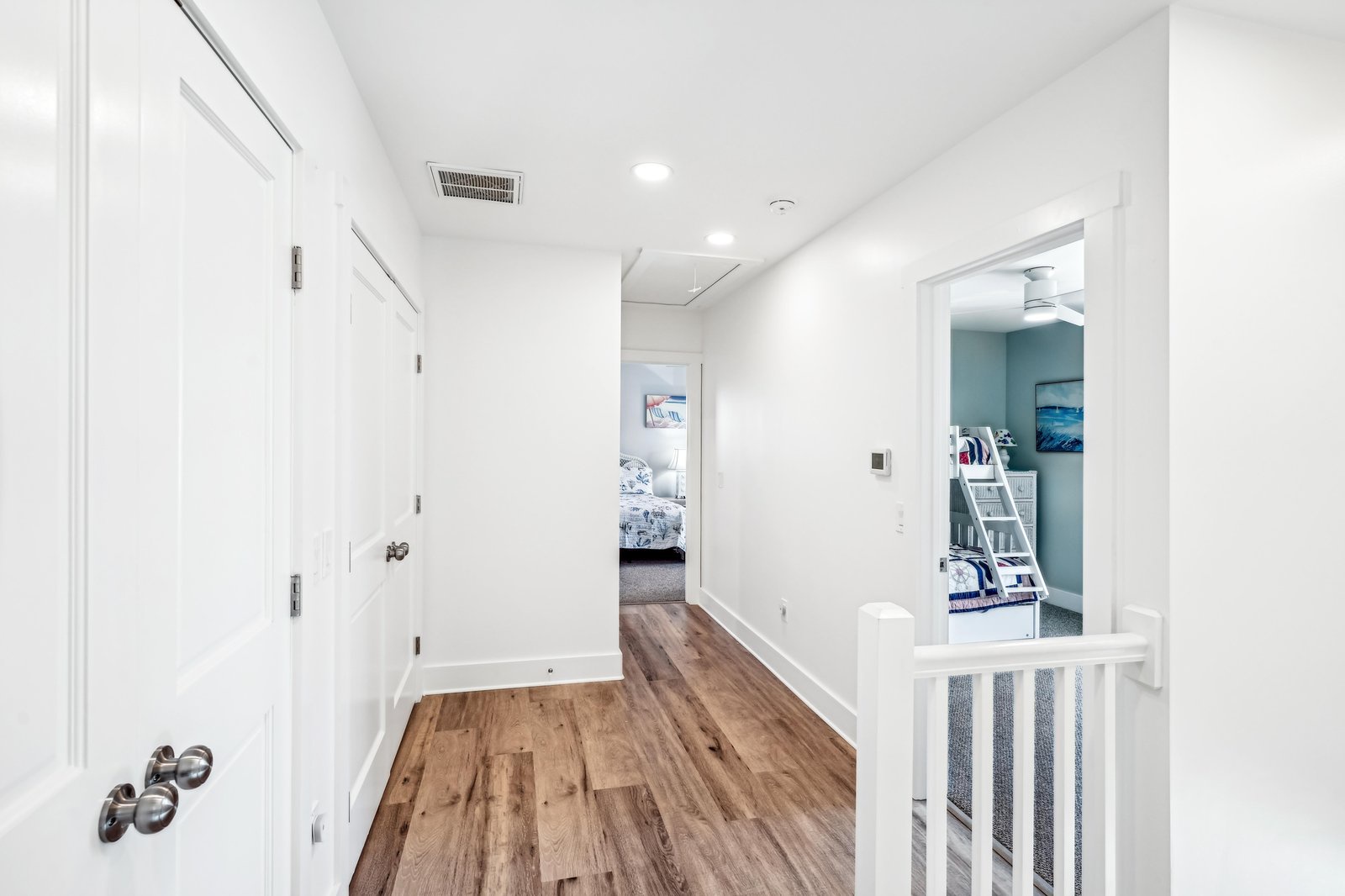 A bright, open hallway with warm wood floors leads you to comfortable sleeping quarters, where bunk beds and coastal-inspired decor await your family.