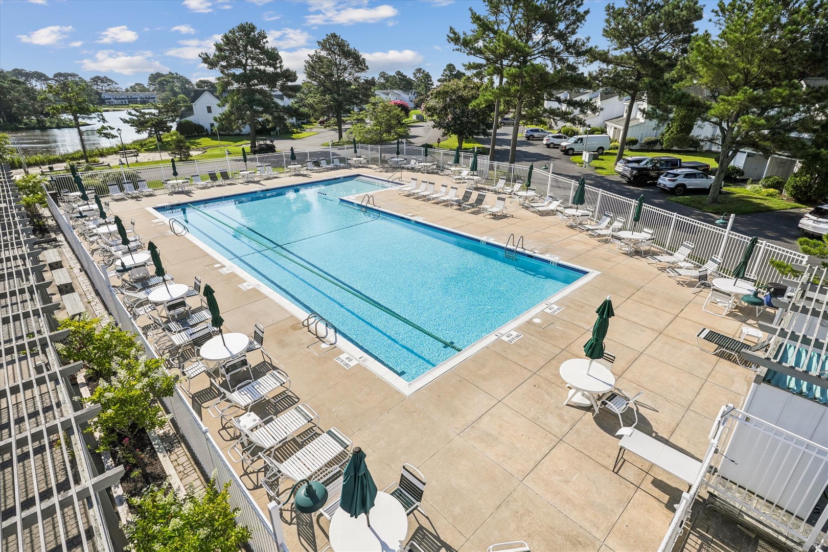 Aerial view of the outdoor swimming pool area, surrounded by spacious deck, lounge seating, and views of the nearby waterfront and neighborhood.