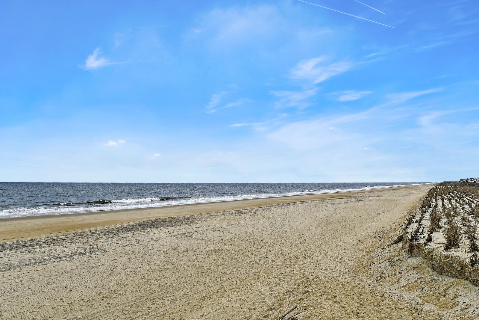 A pristine stretch of sandy shoreline meets calm ocean waters under a brilliant blue sky—your perfect coastal escape awaits nearby.