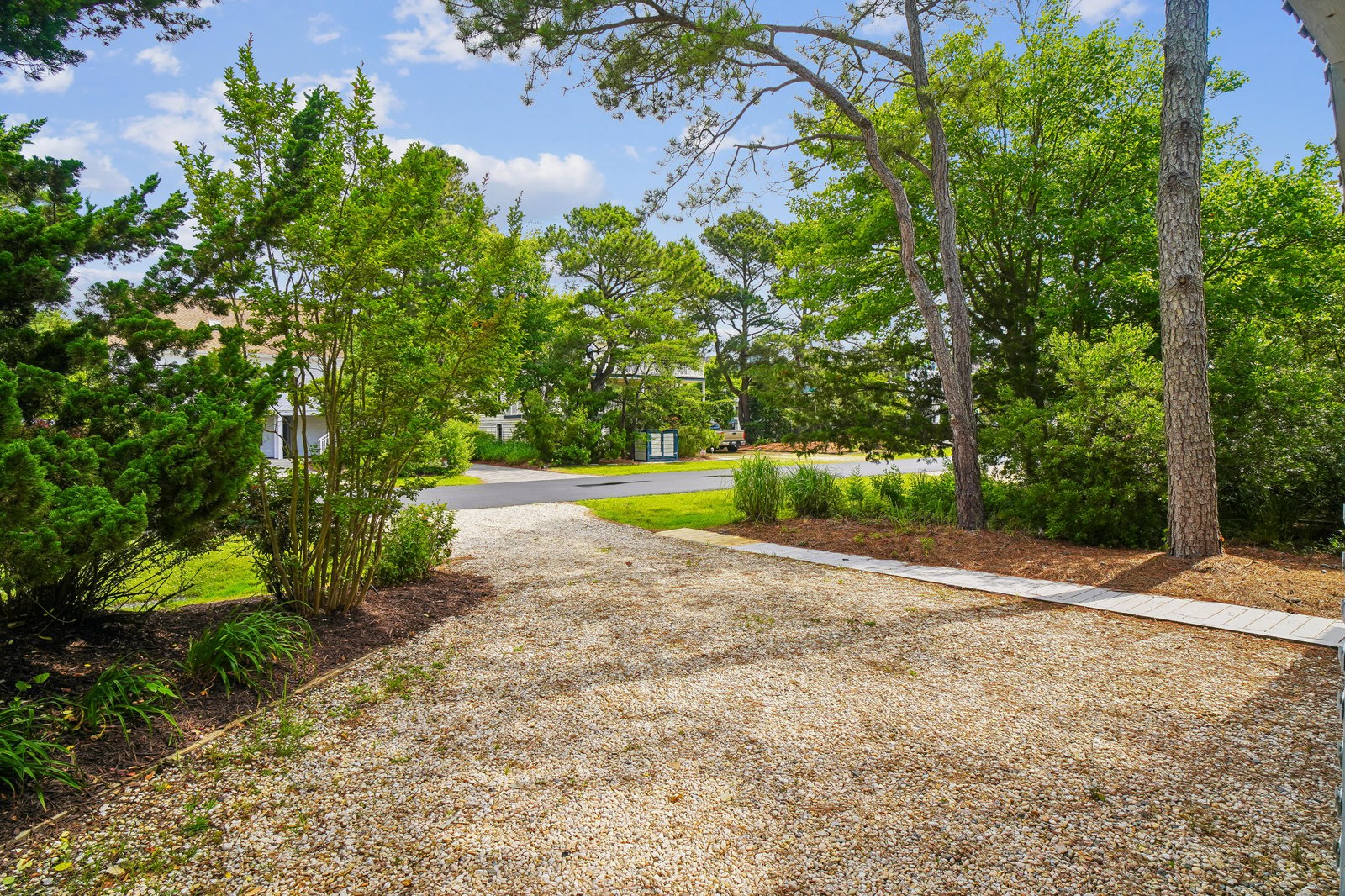 A scenic gravel driveway winds through lush greenery and towering trees, offering a peaceful approach to this private retreat nestled in a quiet neighborhood.