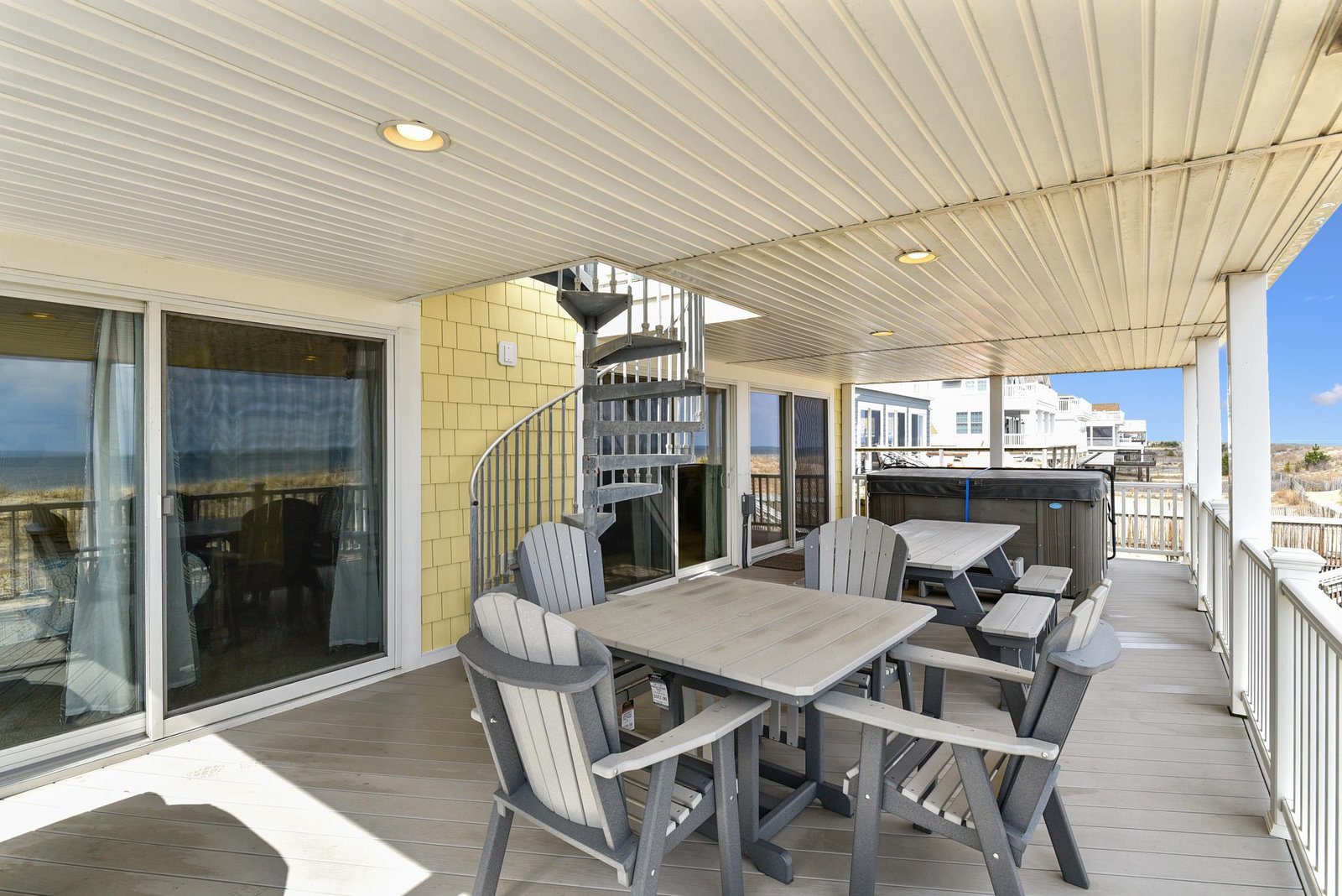 This expansive covered deck offers comfortable outdoor dining with ocean views visible in the distance. The spiral staircase connects to upper or lower levels, giving you easy access to more of this coastal retreat.