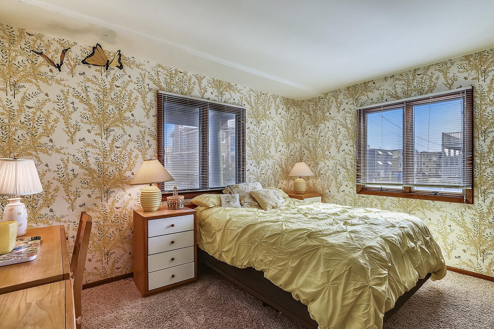 Sink into this cozy bedroom adorned with charming botanical wallpaper, where natural light streams through large windows and comfortable furnishings invite restful sleep.