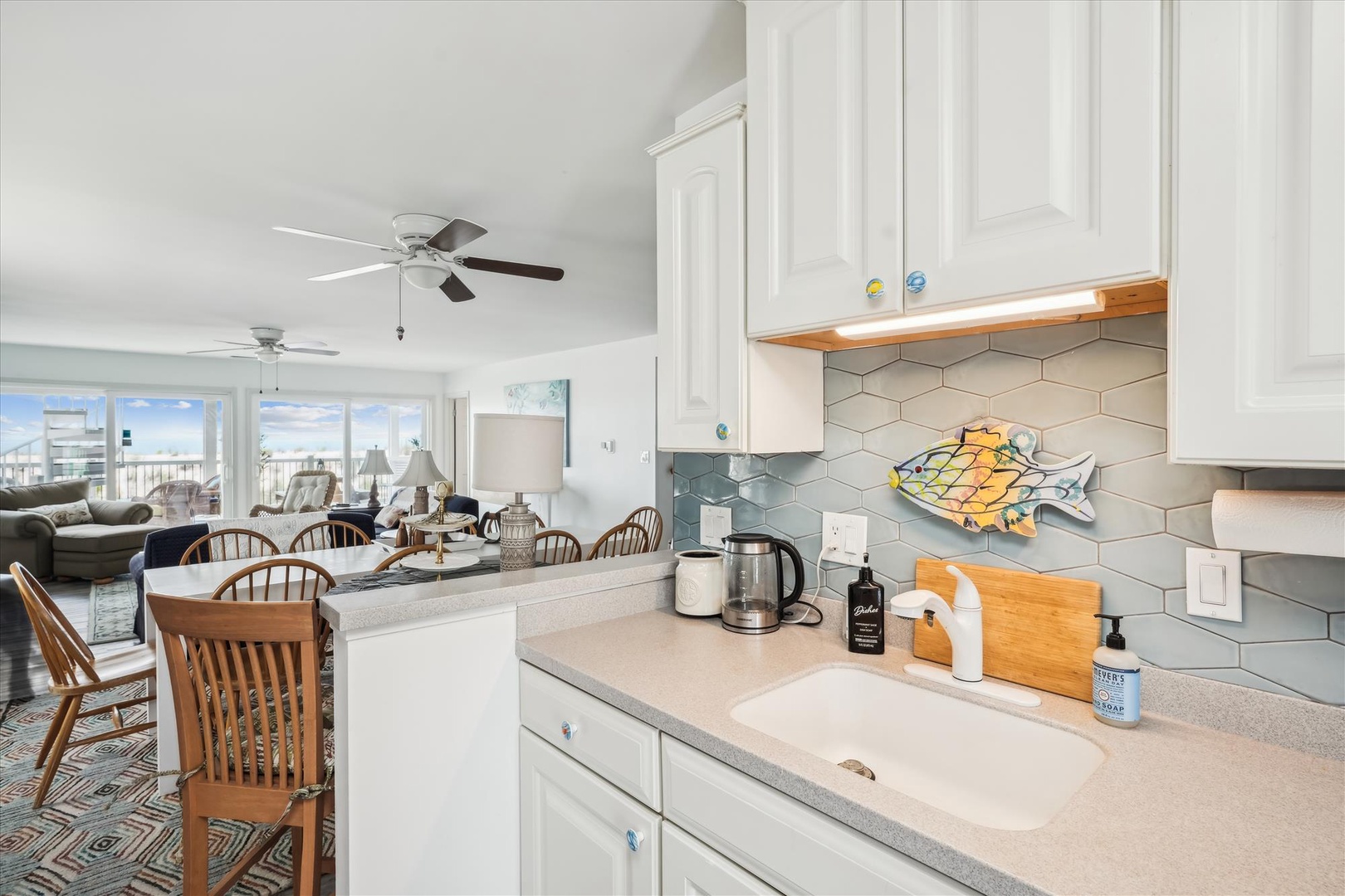 Prepare your favorite meals in this bright, fully equipped kitchen with coastal charm and modern finishes, while glimpsing the ocean view beyond.