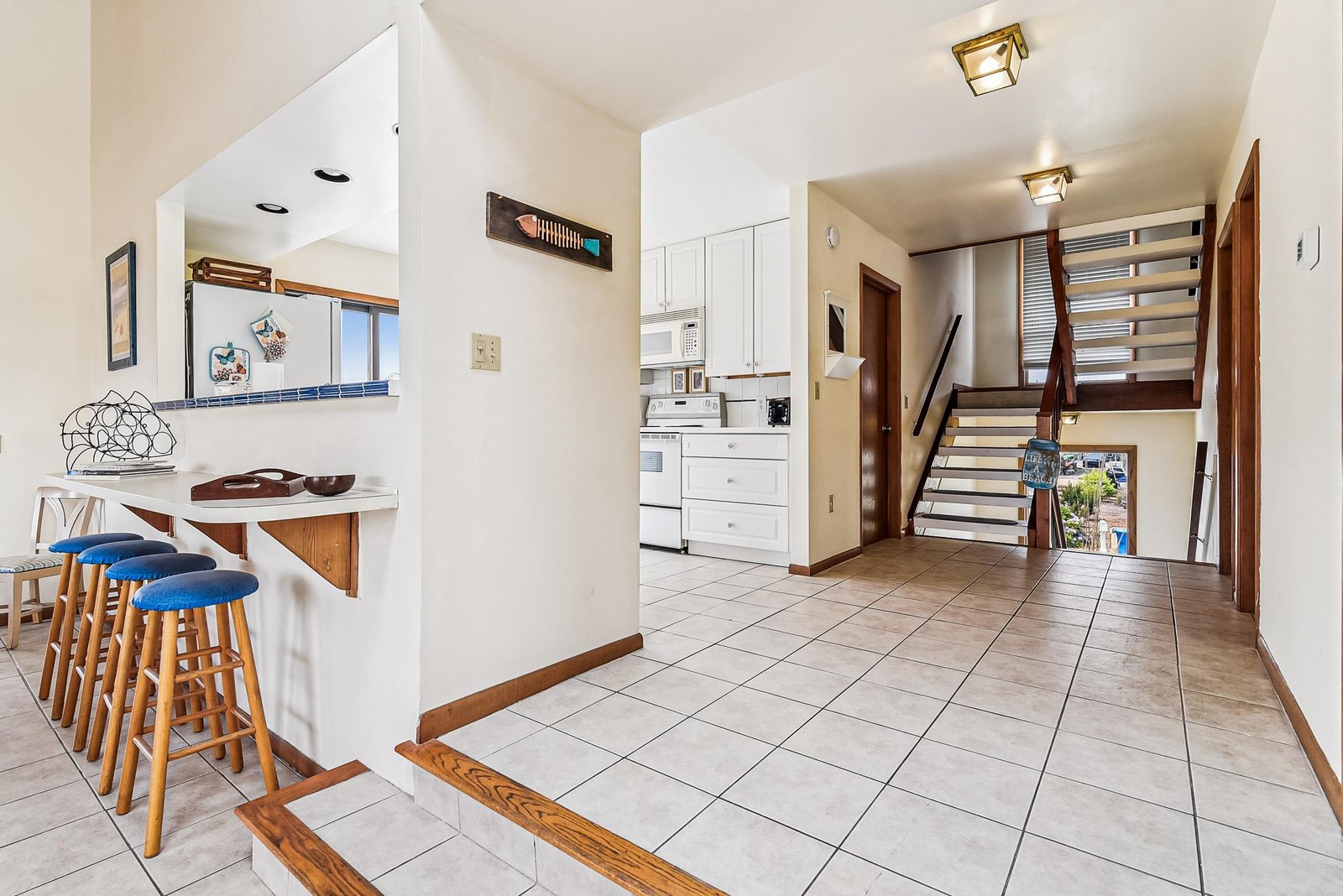 Step into your bright, open-plan space where the kitchen flows seamlessly into a cozy breakfast bar, and the staircase leads up to your private retreat above.