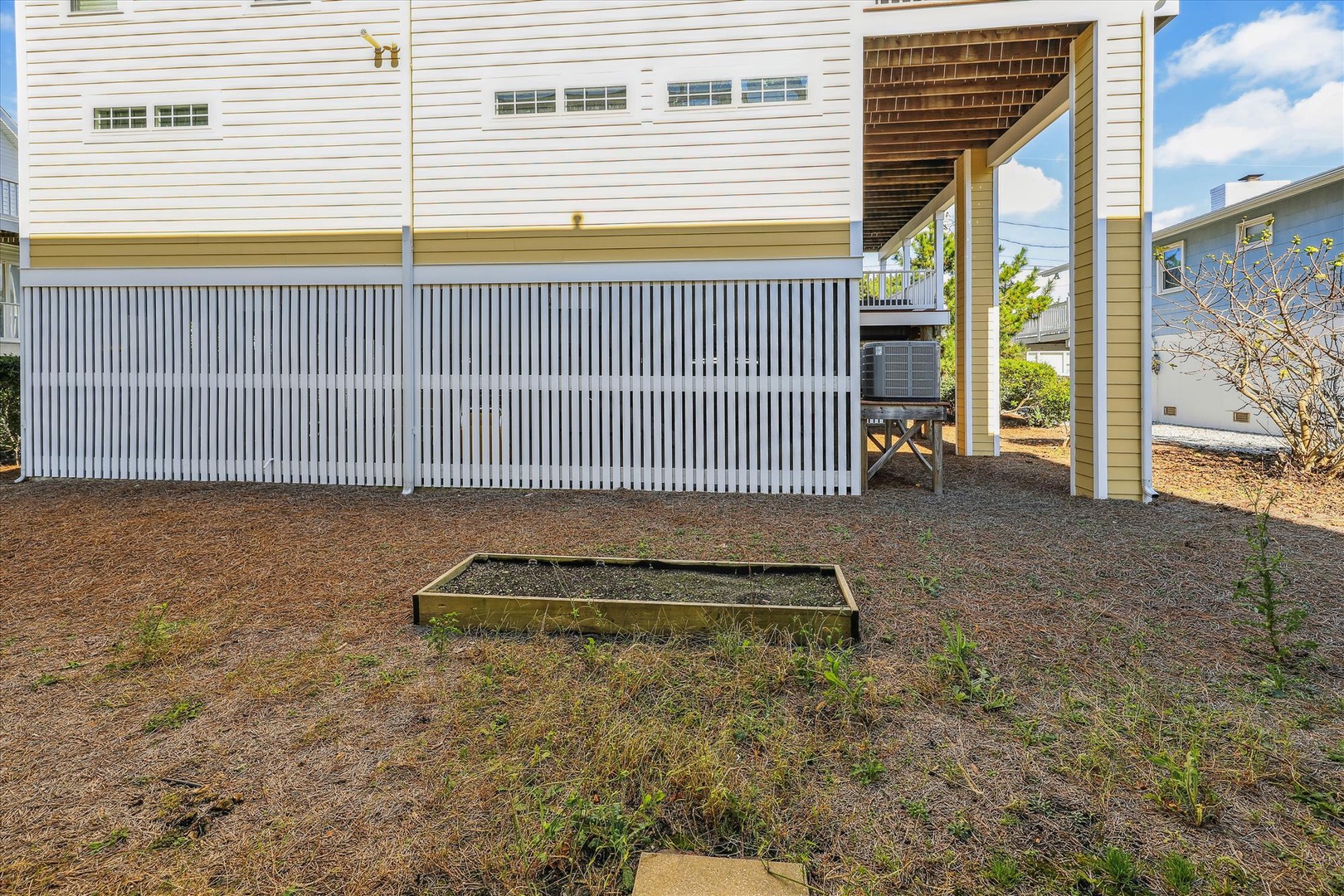 The property features an elevated design with covered parking underneath and a raised outdoor garden bed area surrounded by residential structures.