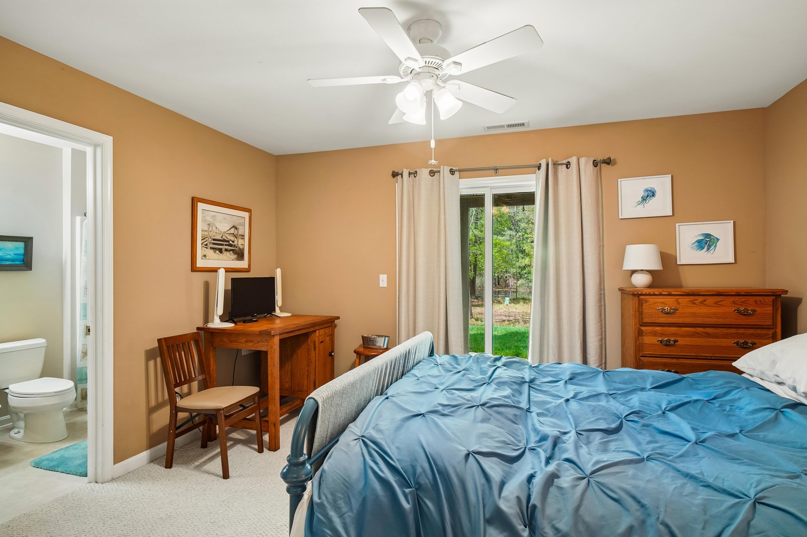 Unwind in your serene bedroom with plush bedding, warm furnishings, ceiling fan, and peaceful garden views through sliding glass doors—your perfect retreat awaits.