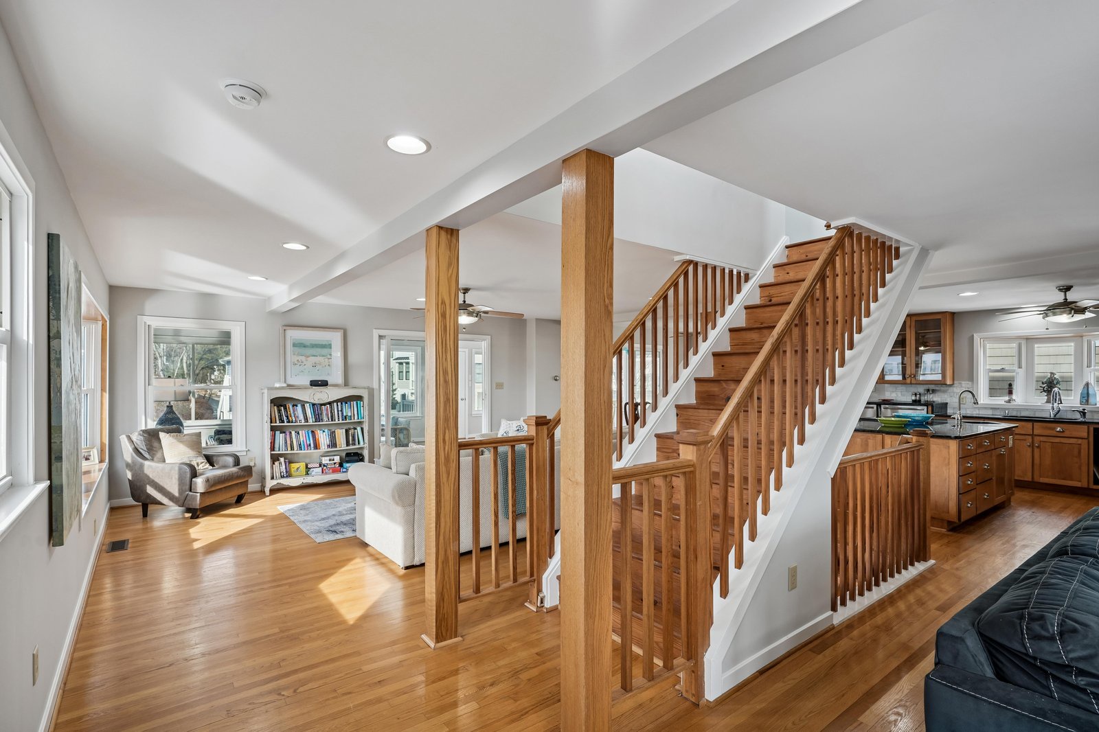 Sunlight pours through expansive windows, highlighting rich wood floors and a stunning staircase that connects your living spaces. The open layout flows from cozy seating to your full kitchen—perfect for gathering.