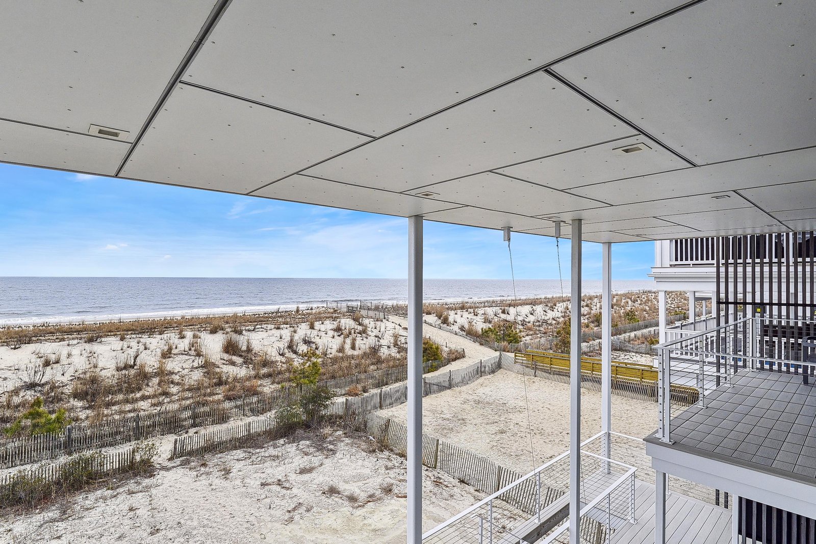 A covered deck frames sweeping ocean views and sandy dunes, with direct beach access just steps away—your coastal retreat awaits.