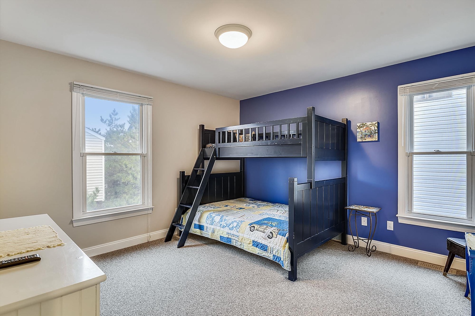 Spacious bedroom featuring a stylish navy bunk bed, perfect for kids or groups. Bright windows fill the room with natural light, creating a cozy retreat.