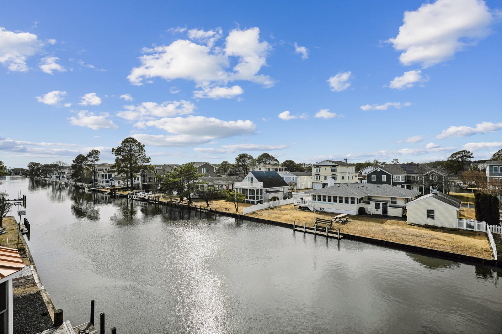 Aerial view of a serene waterfront neighborhood with private docks, nestled along calm canals under a bright blue sky dotted with fluffy clouds.