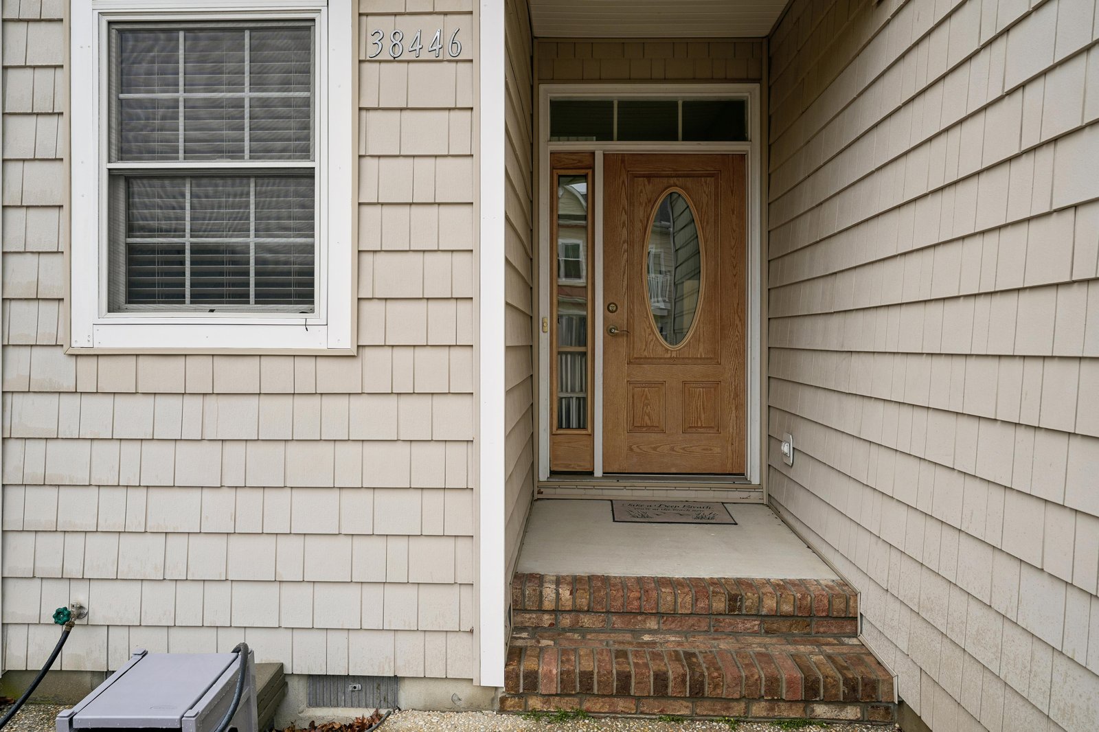 Property at 38446 features a welcoming front entrance with wood-finish door and decorative glass panel, framed by neutral shake siding.