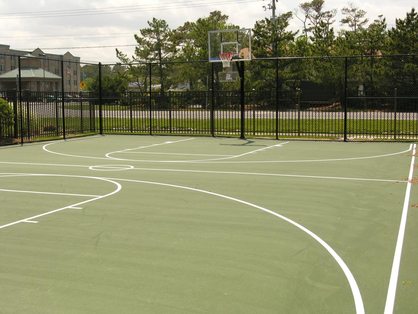 Full-sized outdoor basketball court surrounded by mature trees and residential neighborhood, ready for pickup games and active recreation.