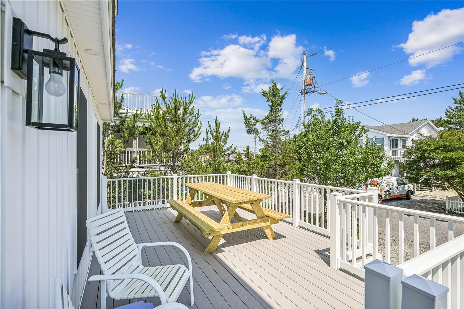Spacious deck with picnic table and seating, surrounded by lush greenery in a peaceful neighborhood setting.