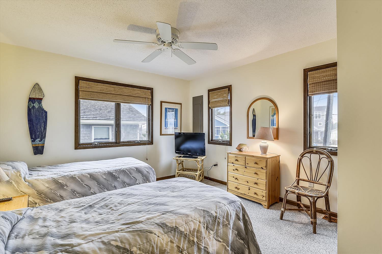 Your cozy coastal bedroom features comfortable twin beds with soft linens, natural woven window shades, and charming nautical decor that sets the perfect beach house mood.