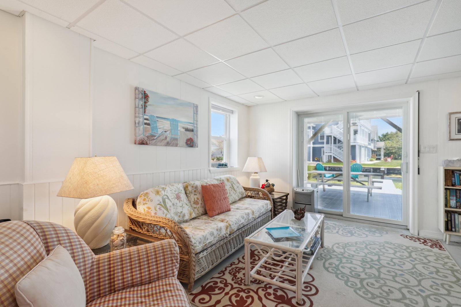 Settle into your cozy living room with wicker charm and bright coastal light streaming through glass doors to your private deck. The perfect spot to unwind after beach days.
