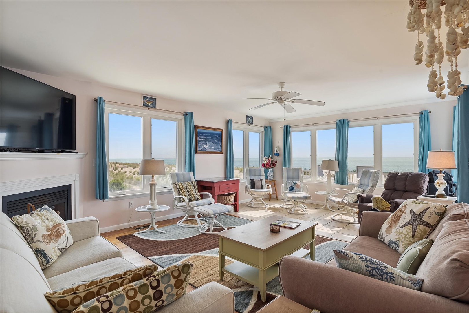 Picture yourself unwinding in this bright, coastal living space with sweeping ocean views through floor-to-ceiling windows. Relax by the fireplace or gather with loved ones on comfortable seating while enjoying stunning seaside vistas.