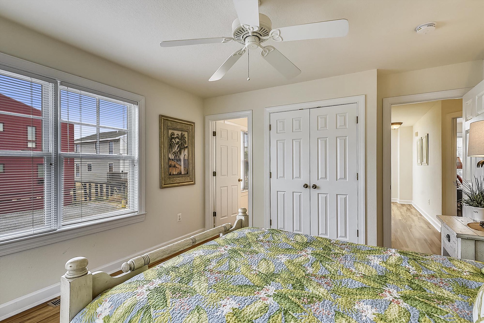 Drift off in your cozy bedroom, cooled by gentle ceiling fan breezes and bathed in natural light from large windows. The soft quilt and warm tones create a restful retreat.