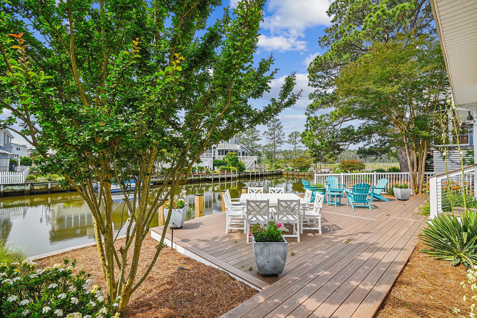 Picture yourself relaxing on this spacious waterfront deck, sipping morning coffee in the turquoise chairs while gentle breezes drift across the canal. Lush trees provide natural shade as you gather with loved ones at the outdoor dining table, creating un