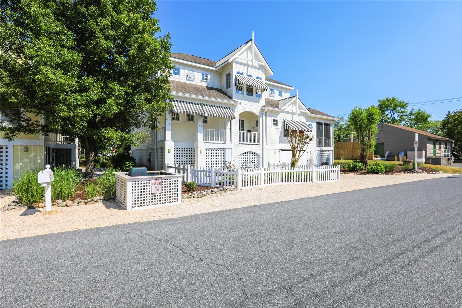 Charming multi-level vacation rental with classic coastal architecture, striped awnings, and welcoming balconies set in a peaceful residential neighborhood surrounded by mature trees.