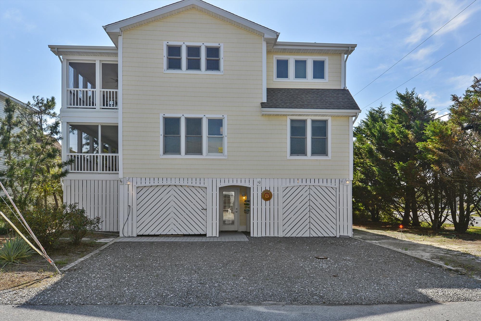 A charming coastal-style property with spacious balconies, modern amenities, and gravel parking, nestled among mature trees in a peaceful neighborhood setting.