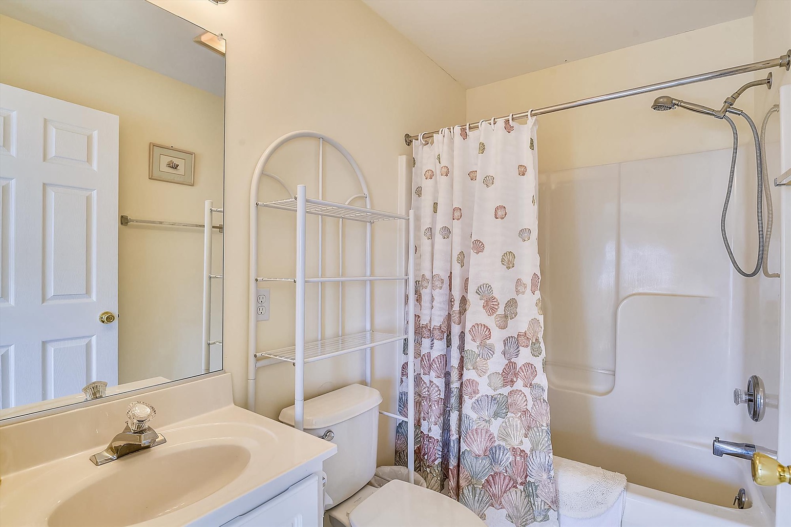 Your private bathroom features a tub-shower combo with coastal-themed curtain, storage shelving, and everything needed for a comfortable stay.
