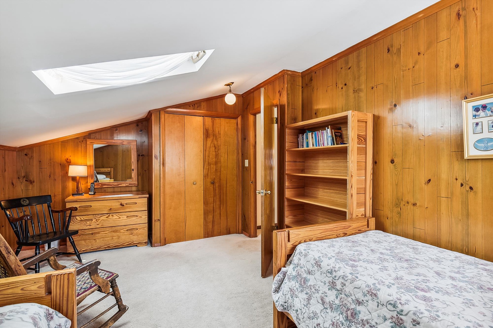 Relax in your charming knotty pine bedroom with vaulted skylight and cozy furnishings. Enjoy the warm wood tones, built-in bookshelf, and inviting rocking chair.