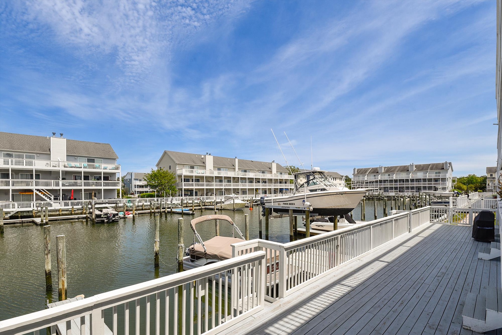 A spacious waterfront deck overlooks a serene marina with boats docked at your doorstep, offering stunning views of the surrounding coastal community under a bright blue sky.