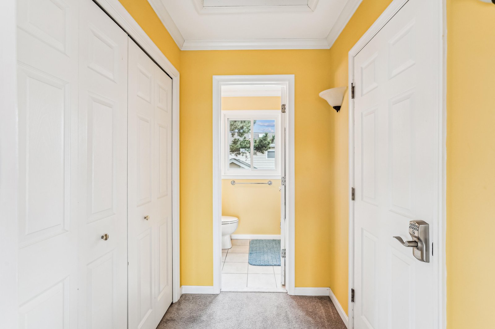 Step into cheerful sunlit spaces where bright yellow walls welcome you with warmth. The bathroom beyond offers crisp tiled floors, natural light, and plenty of thoughtful storage.