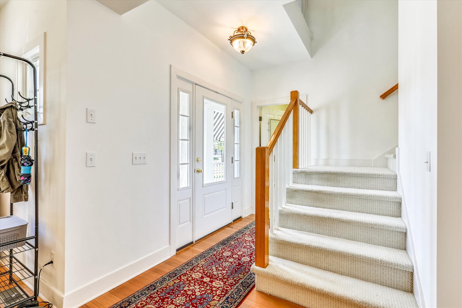 Step into your welcoming entryway with gleaming hardwood floors, elegant light fixture overhead, and bright natural light streaming through the glass-paneled door.