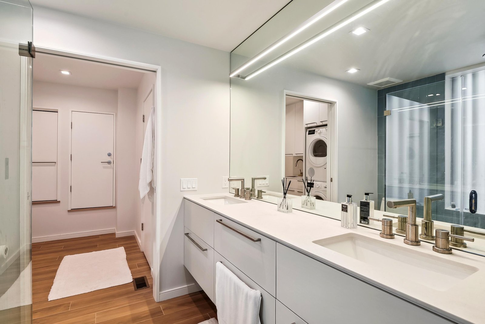 Step into your sleek, modern bathroom with dual sinks, a spacious vanity, and warm wood floors that add a touch of home. Your personal in-suite washer and dryer wait just beyond, making your stay effortless.
