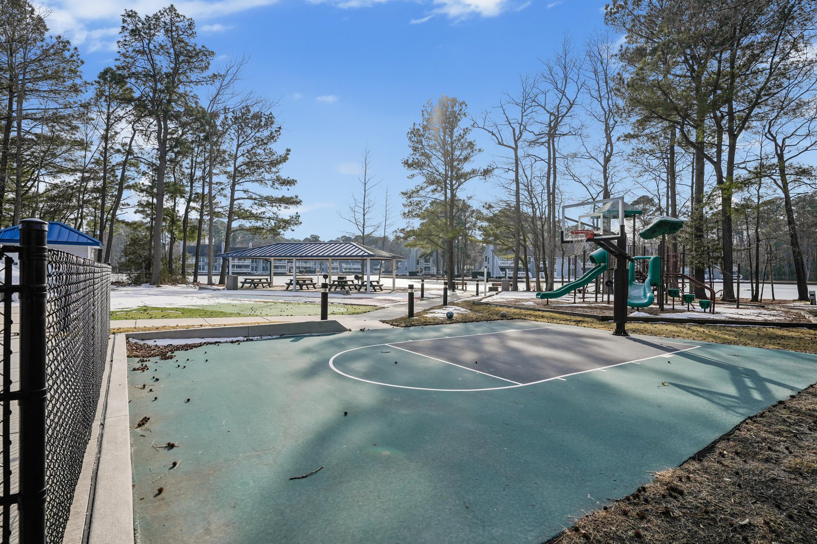 Community basketball court with playground, picnic areas, and adjacent rental homes set among tall pines in a peaceful wooded neighborhood.