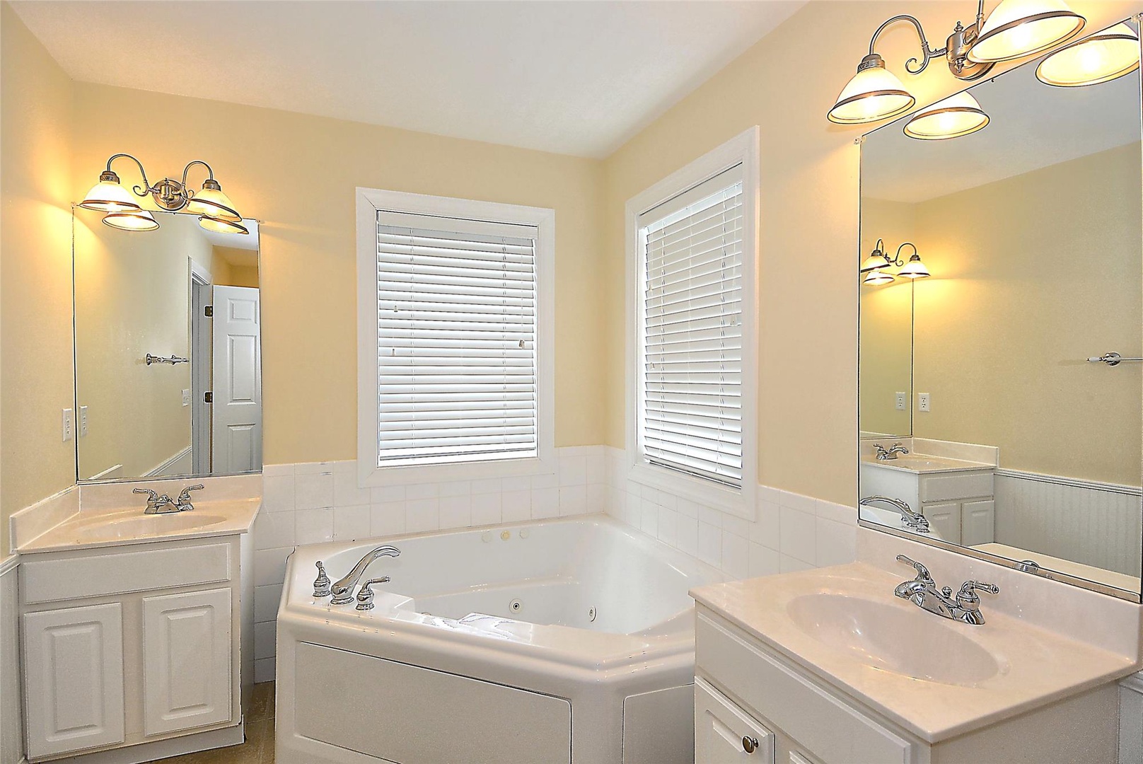 Unwind in your spacious bathroom featuring dual vanities, a luxurious soaking tub, and warm natural light streaming through plantation shutters.