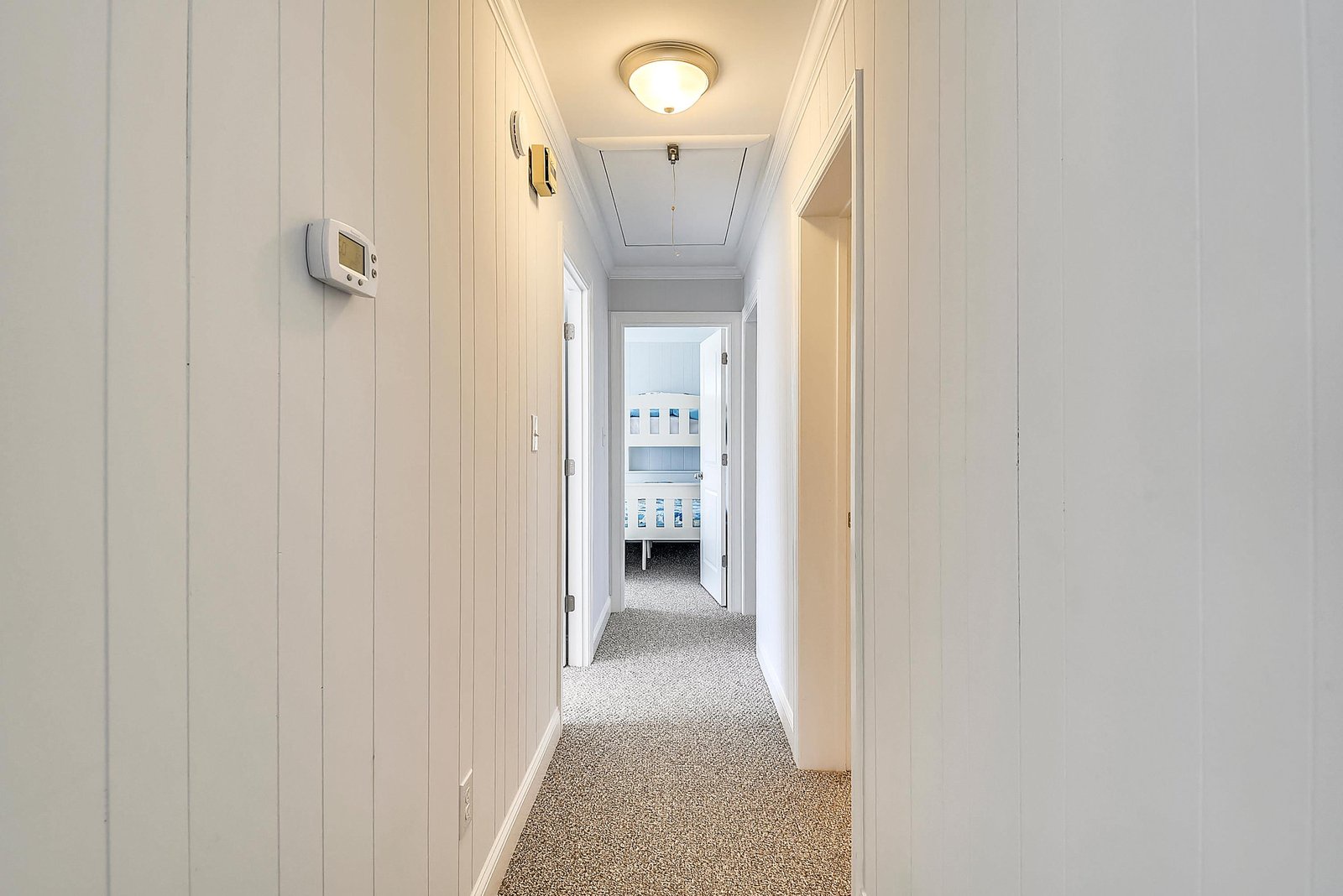 Clean lines and crisp white paneling guide you toward restful bedrooms, where comfort and coastal charm await your arrival.