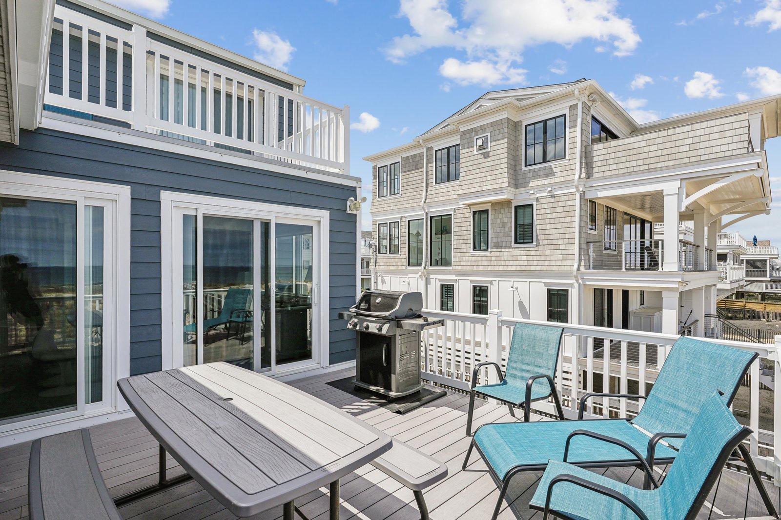 The property sits in a charming waterfront neighborhood, surrounded by classic coastal architecture and neighboring beach houses under clear blue skies.