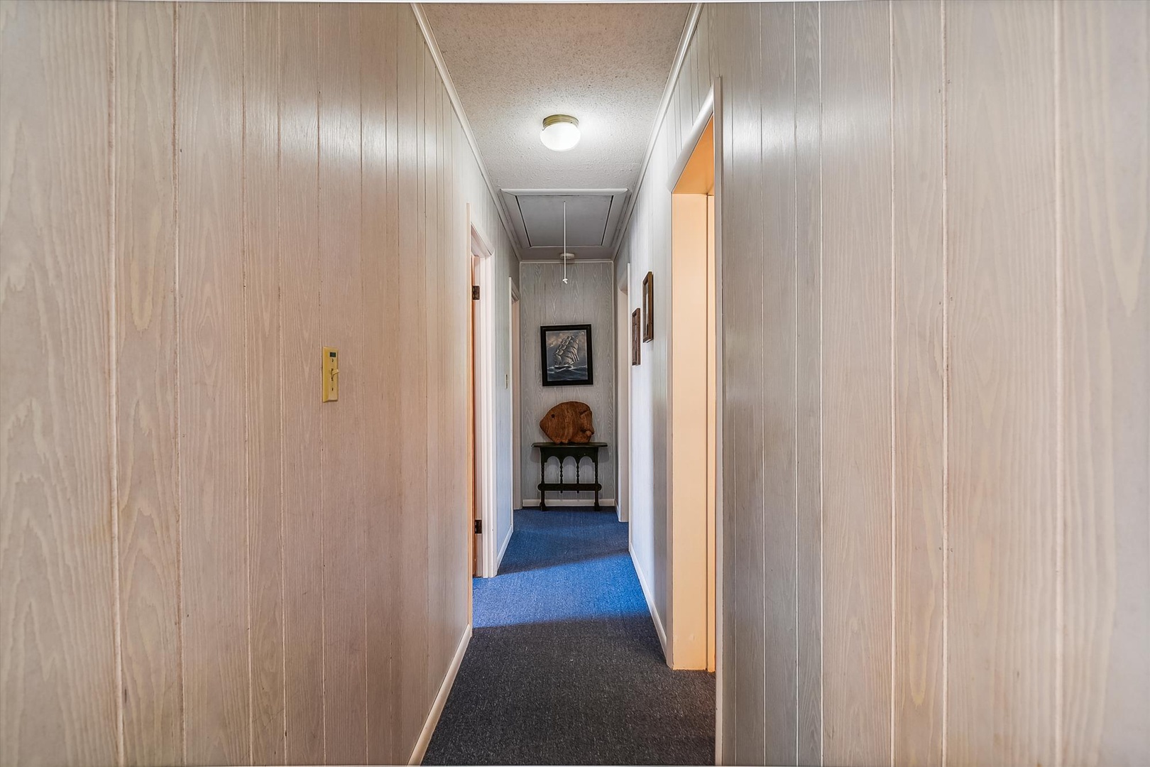 This hallway leads you to your private retreat, with charming wood-paneled walls and thoughtful touches like artwork and a welcoming bench, creating a cozy, homey feel throughout your stay.