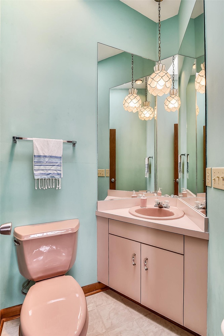 Refresh and recharge in your own charming bathroom, where soft turquoise walls meet retro pink fixtures and warm pendant lights create a cozy, welcoming glow for your morning routine.