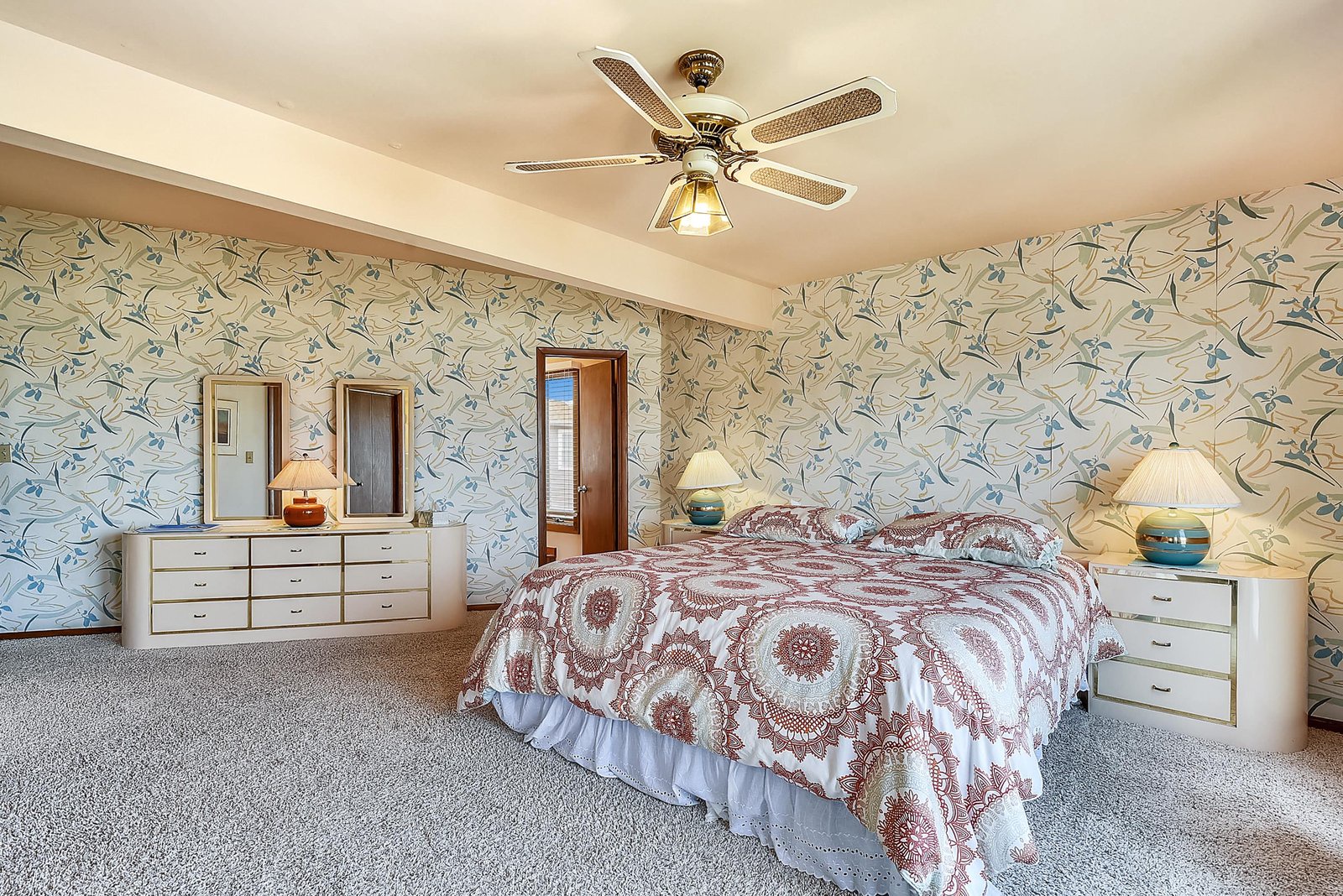 Drift off in a spacious bedroom with charming floral wallpaper, soft carpet underfoot, and a ceiling fan to keep you cool and comfortable all night long.