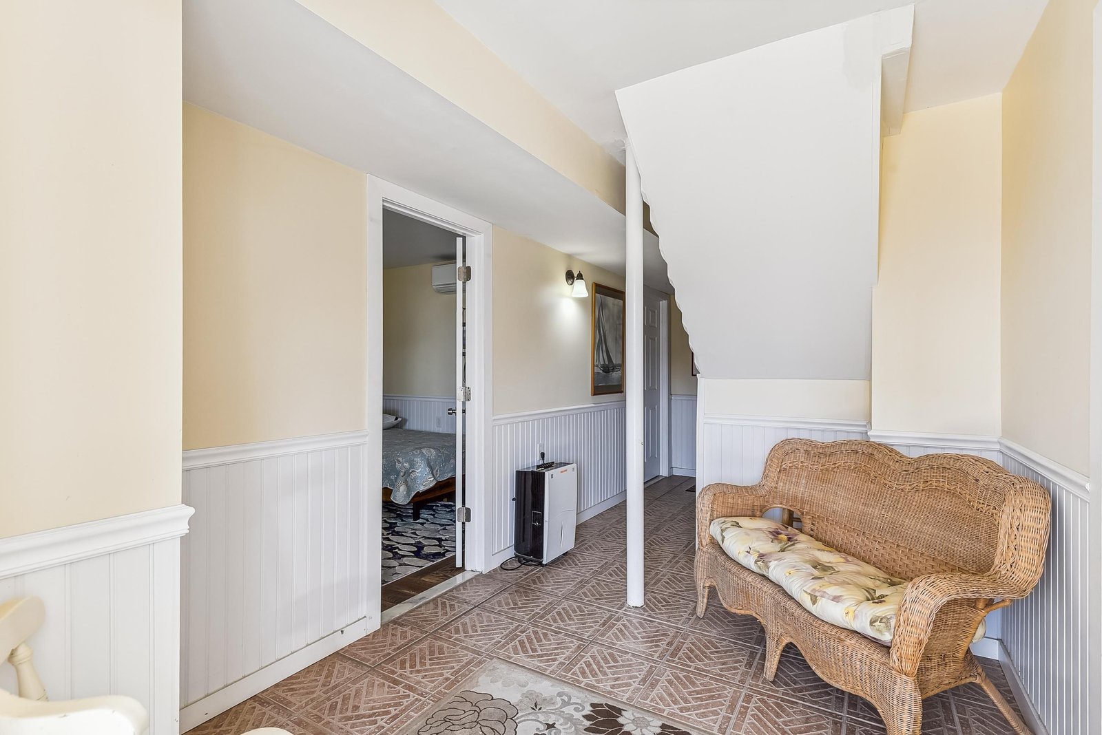 Your cozy upstairs retreat features charming wicker seating and cottage-style wainscoting, creating a welcoming nook to relax and unwind.