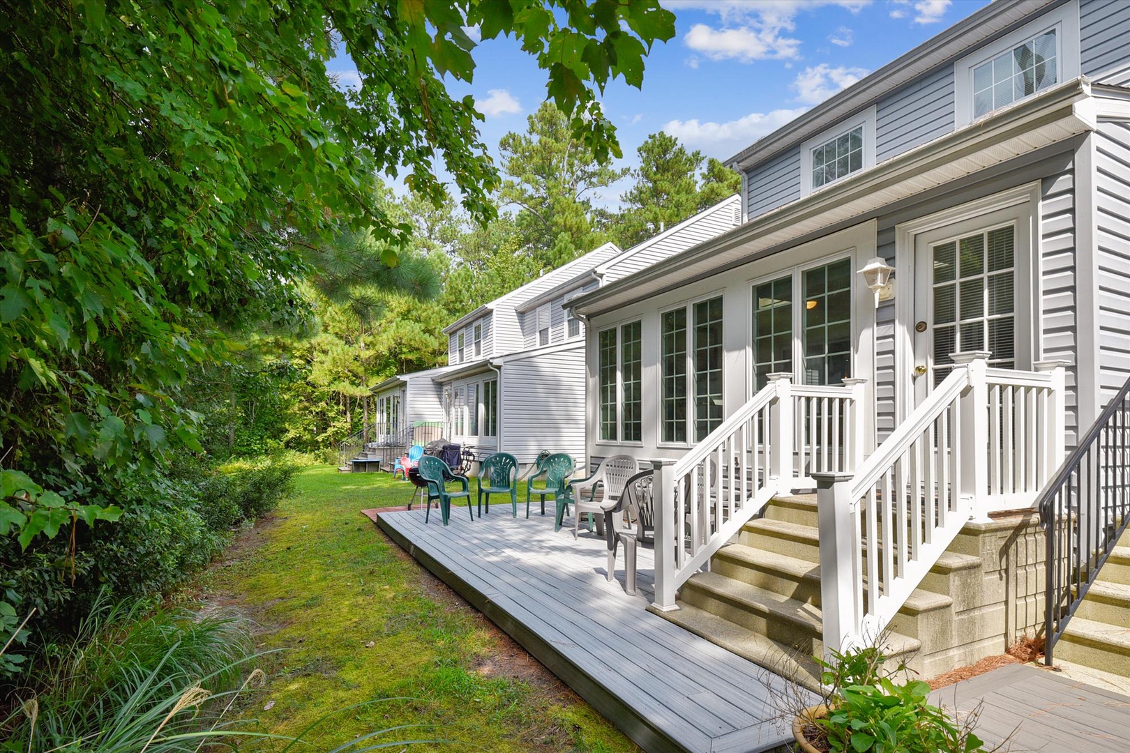 A welcoming property nestled among lush greenery, featuring a spacious deck with comfortable seating for relaxing moments outdoors. The bright blue sky and surrounding trees create a peaceful, private retreat.