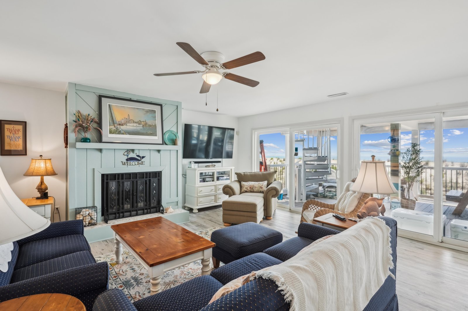 Unwind in this bright coastal living room with soft sofas, cheerful nautical accents, and a comforting fireplace—your perfect spot to relax after a day by the sea.