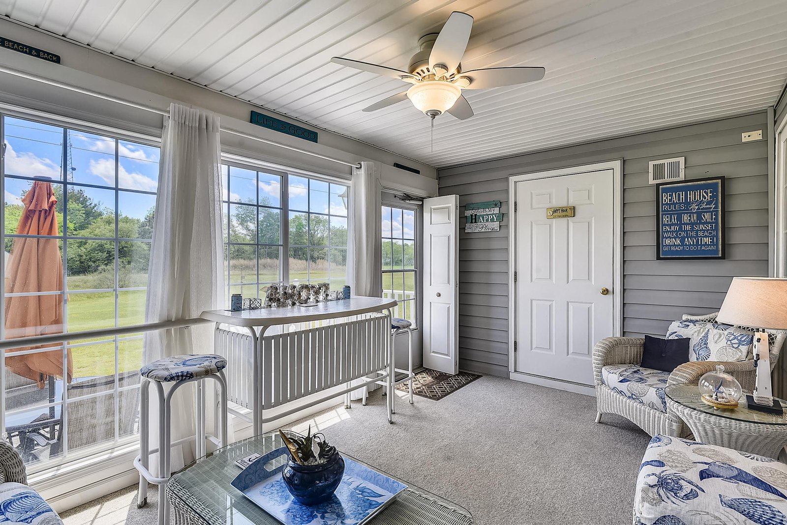 Step into your own cheerful retreat with coastal charm—bright windows frame peaceful views, cozy wicker seating invites you to unwind, and beachy decor welcomes you home.