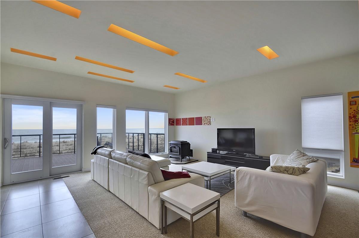 Sink into plush seating as you gaze through expansive glass doors at sweeping coastal views, where contemporary design and natural beauty frame your perfect retreat.