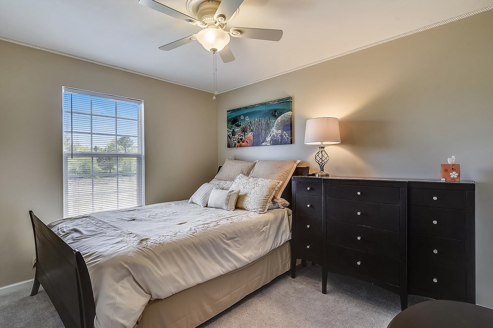 Relax in your tranquil bedroom featuring a plush queen bed, coastal artwork, and warm natural light—your peaceful retreat awaits.