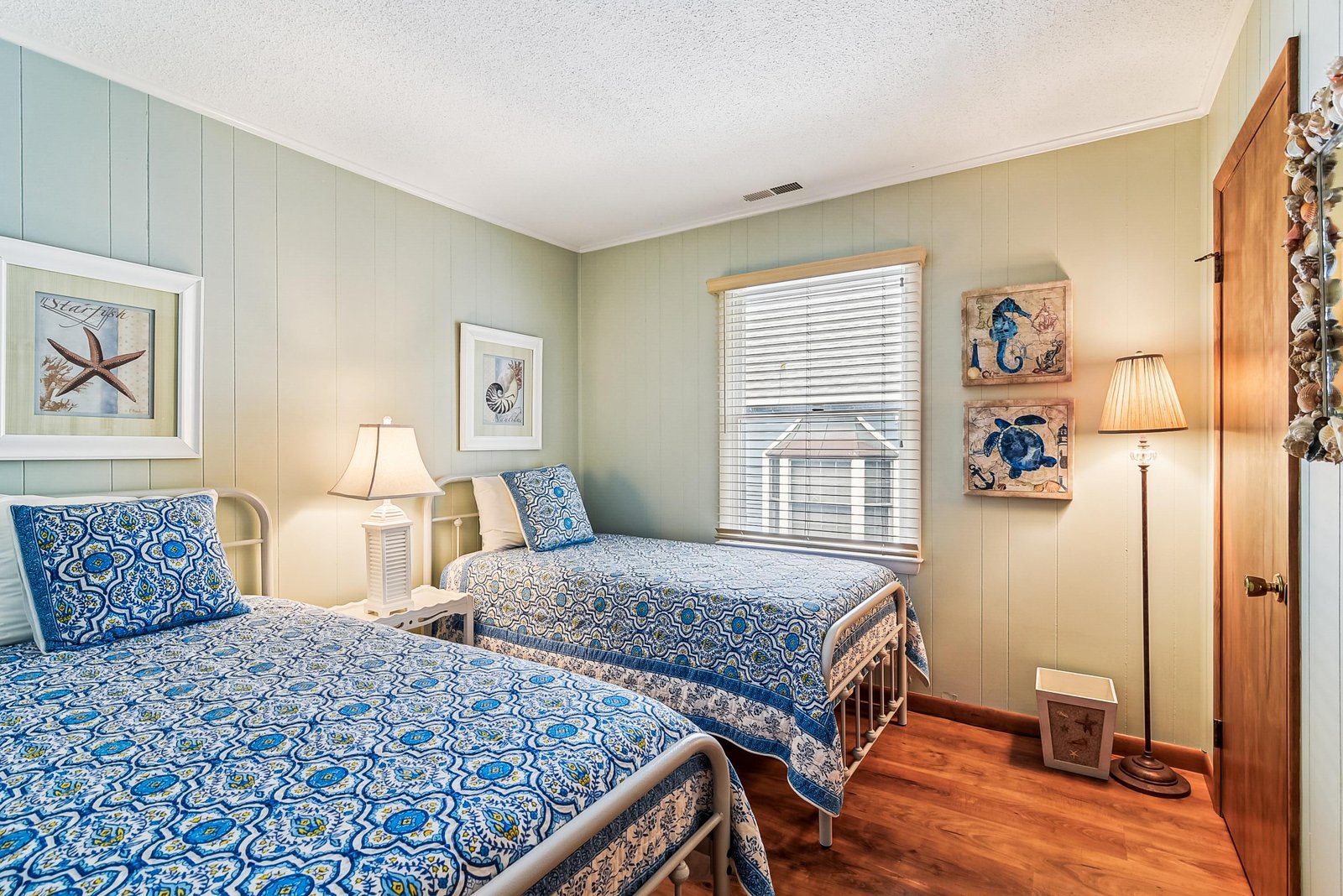 Two cozy beds dressed in coastal blues invite you to unwind after sun-soaked days at the shore, with charming nautical touches and soft lighting setting the tone.