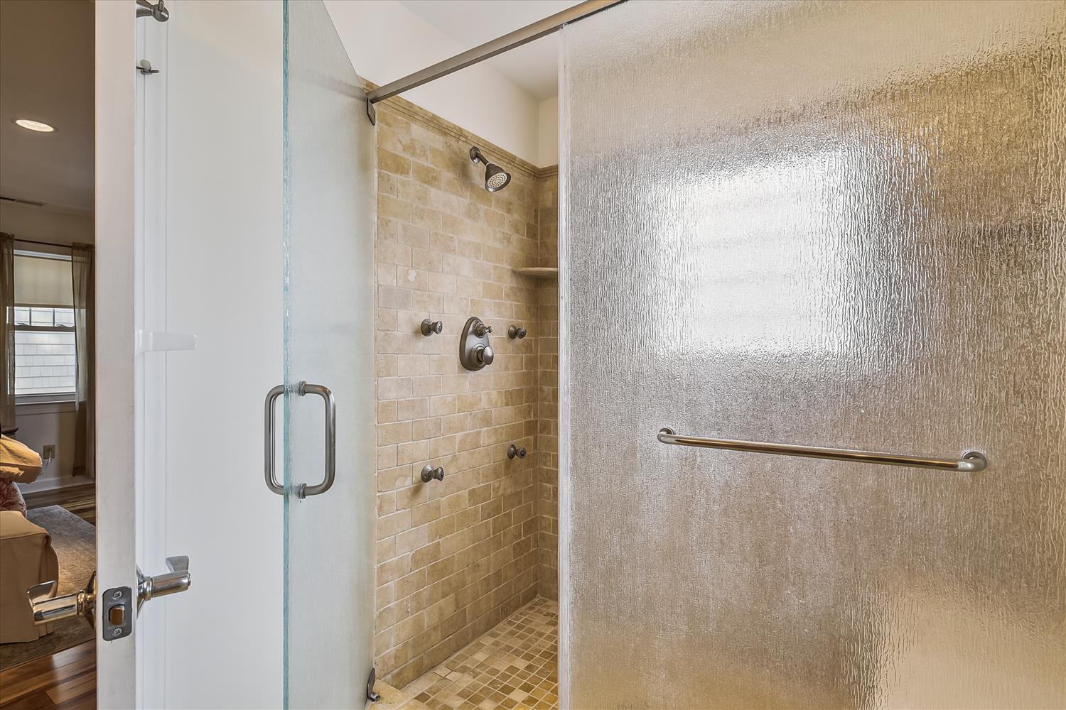 Step into your private spa-like shower featuring warm tile and multiple body jets, plus a handy grab bar. The glass enclosure keeps the space bright and open.